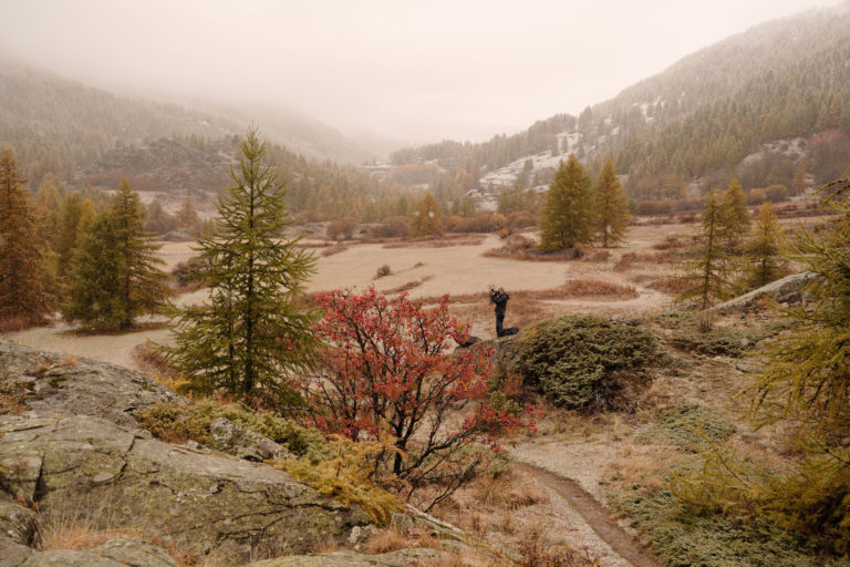 Photographe sous la neige – Vallée de la Clarée Photographe en train de cadrer un paysage automnal sous une fine neige dans la vallée de la Clarée, Hautes-Alpes